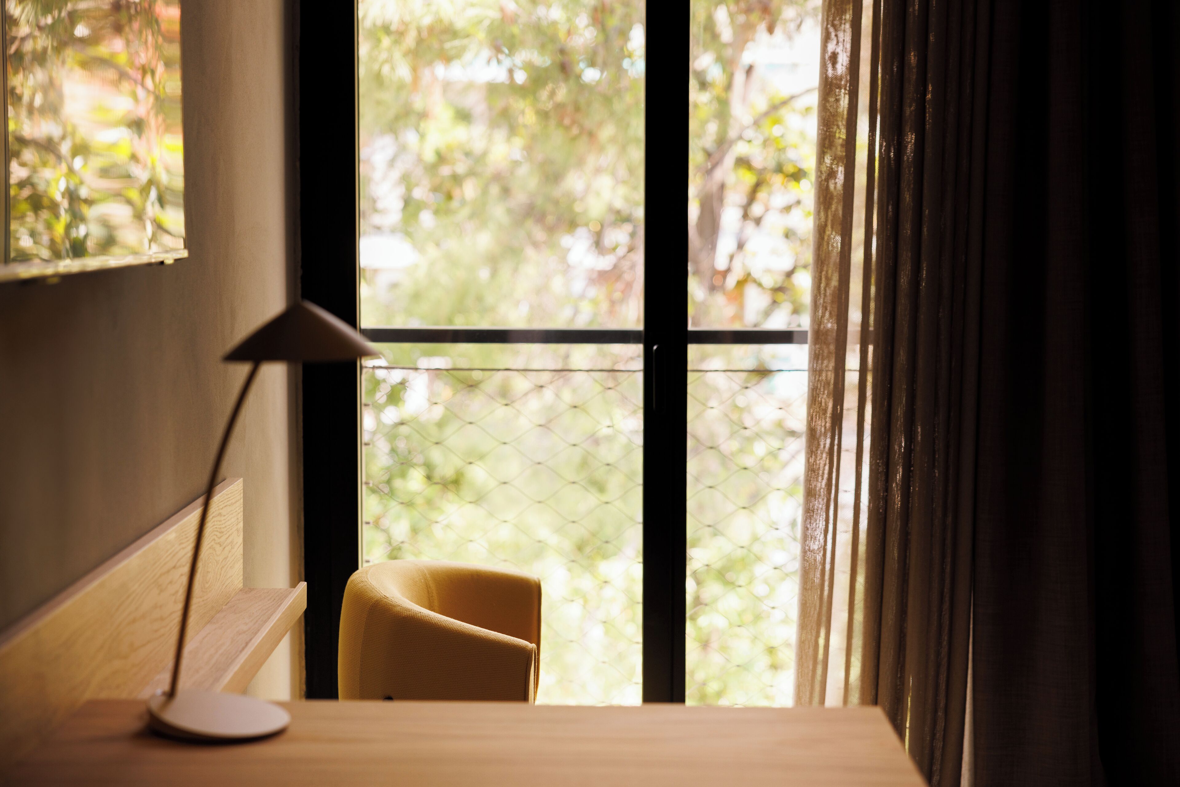 A room with a desk, a chair, a lamp, and a window with a view of greenery.
