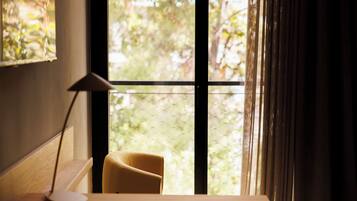 A room with a desk, a chair, a lamp, and a window with a view of greenery.
