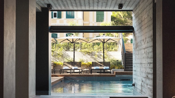 Habitación de hotel moderna con vistas a una piscina exterior, sillas de descanso y sombrillas.