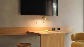 Une chambre moderne avec un bureau en bois, un tabouret, une chaise jaune et un téléviseur à écran plat fixé au mur.