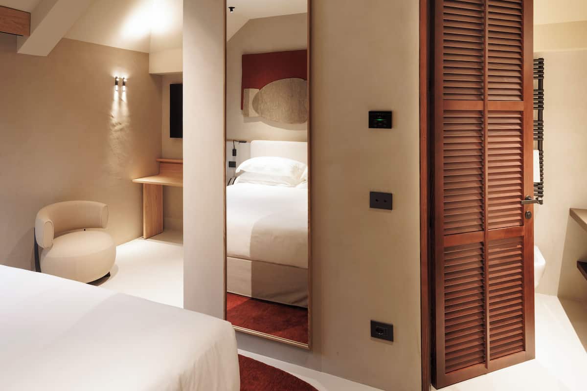 A modern bedroom with a large mirror, a bed, a chair, and a wooden wardrobe.