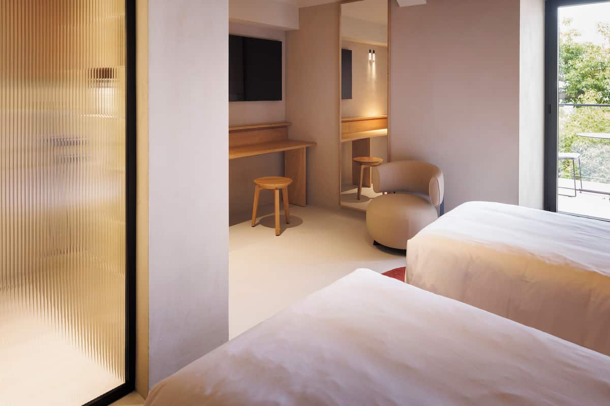 A modern hotel room with a large window, a flat-screen TV, a desk with a chair, and two beds.