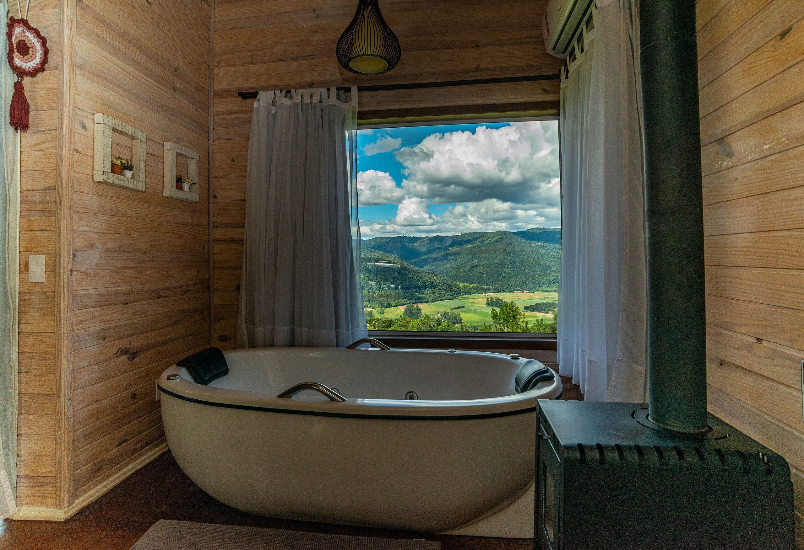 A wooden cabin room with a large bathtub, a wood-burning stove, and a window offering a mountain view.