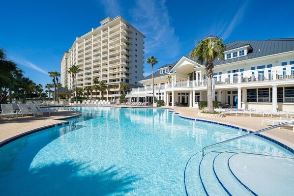 A large swimming pool with lounge chairs and a hotel building in the background.