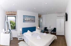 Quarto de hotel moderno com uma cama grande, uma escrivaninha, uma cadeira, um guarda-roupa e um quadro na parede.