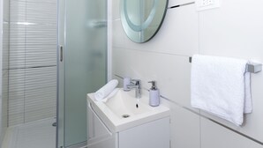 A modern bathroom with a glass shower enclosure, a white sink, and a round mirror.