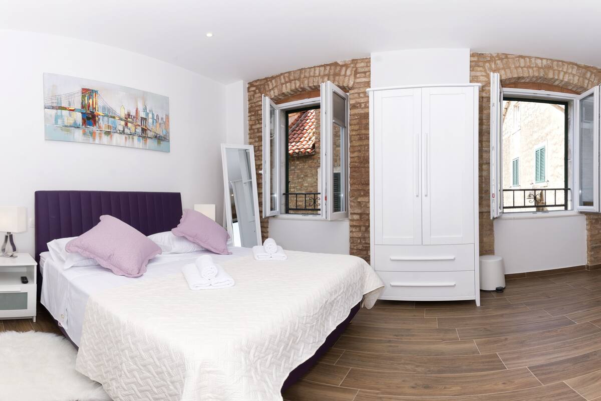 A bedroom with a bed, nightstand, wardrobe, and a painting on the wall.