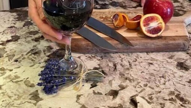 A person holding a wine glass with a dark liquid, a red apple, and a knife on a kitchen counter. - Lavender Farm Private Luxury Suite (South Kingstown)