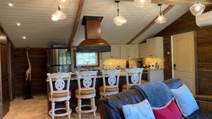 A rustic interior with exposed wooden beams, a stone-tiled floor, a bar area with white chairs, and a sofa with patterned cushions. - Lavender Farm Private Luxury Suite (South Kingstown)