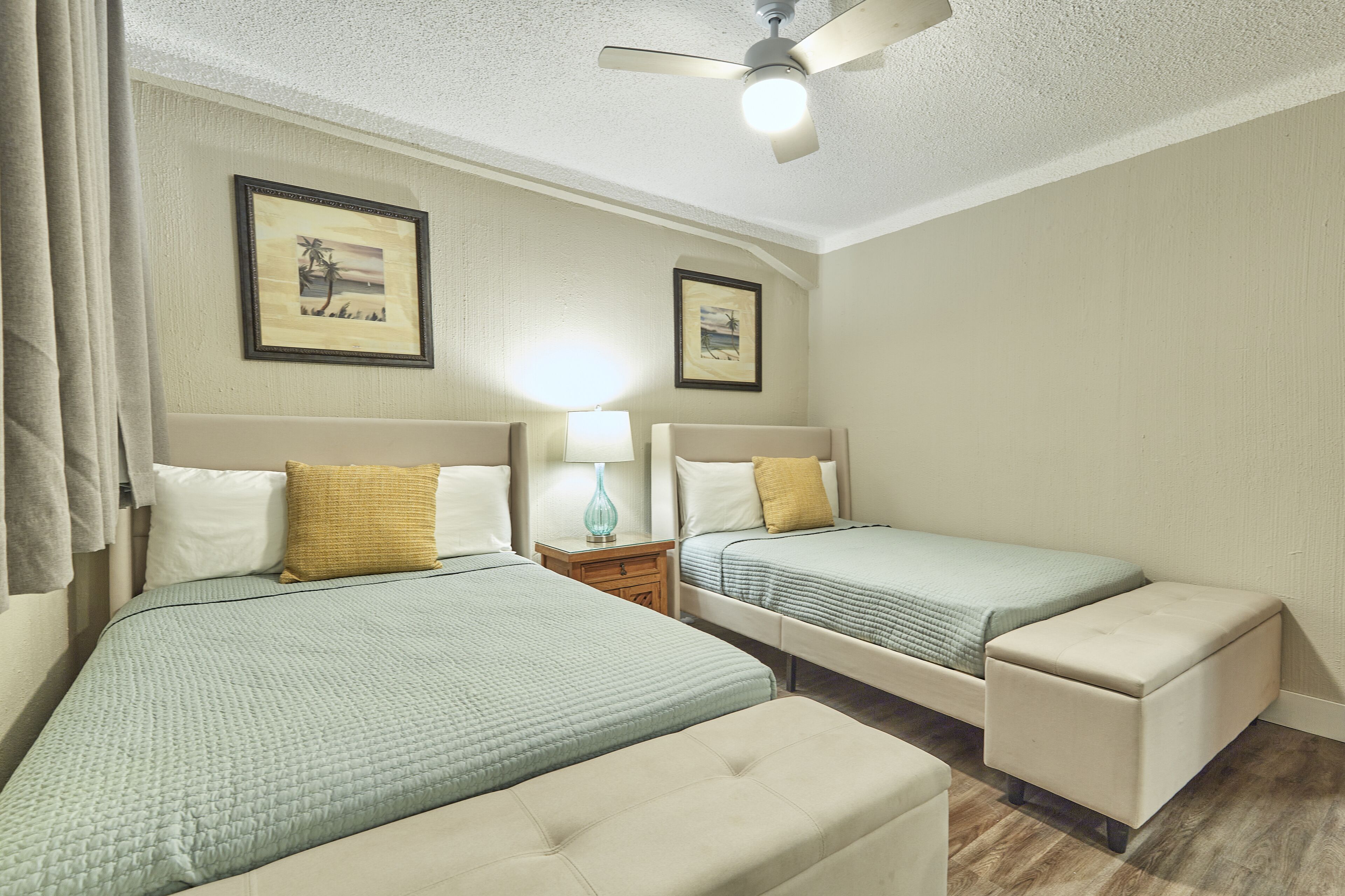 A hotel room with two beds, a ceiling fan, and a nightstand with a lamp.