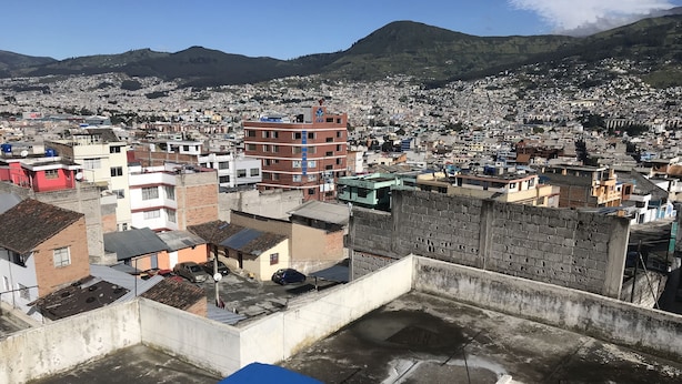A densely packed urban area with a mix of residential and commercial buildings, a prominent hill in the background, and a clear sky. - Suite Toty EN Renta (Quito)