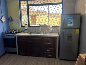 A kitchen with a gas stove, a refrigerator, and a window with a view of a yellow building. - Suite Toty EN Renta (Quito)