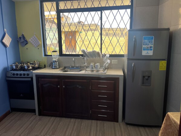 A kitchen with a gas stove, a refrigerator, and a window with a view of a yellow building.