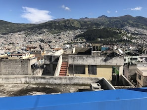 A densely populated urban area with a mix of residential and commercial buildings, a prominent mountain range in the background, and a clear blue sky.