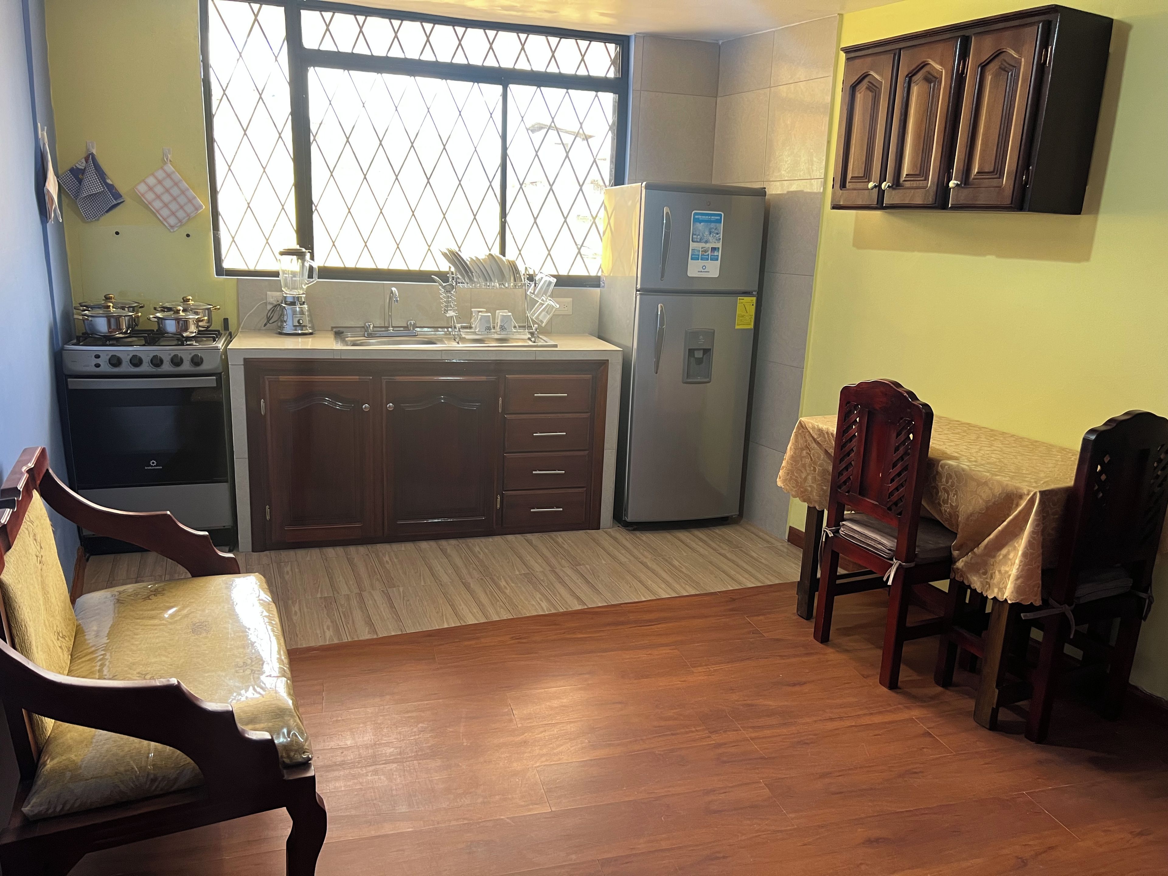 Cocina compacta con estufa, pileta y refrigerador. Hay un comedor con mesa y sillas.