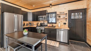 A modern kitchen with stainless steel appliances, a wooden ceiling, and a black door. - Cozy 2BR/1BA cabin for 6. Fireplace, outdoor fire pit, hot tub, and soaking tub. (Norwich)
