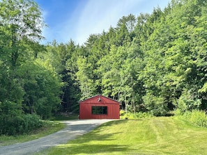 Escape to a serene forest retreat, surrounded by lush greenery and accessible via a winding gravel path.