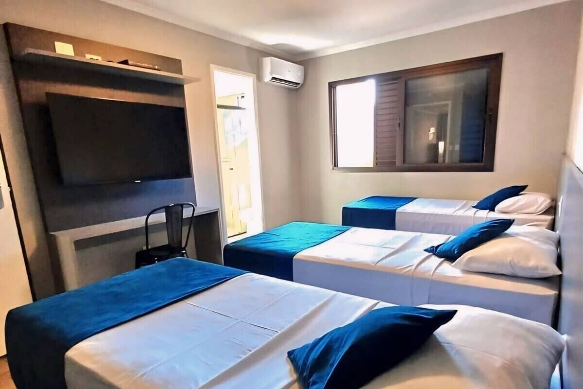Une chambre d’hôtel avec deux lits, un téléviseur fixé au mur, un appareil de climatisation et une fenêtre avec des stores.