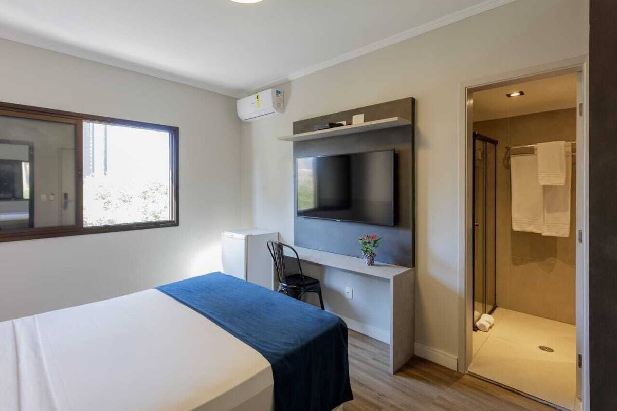 Une chambre d’hôtel moderne équipée d’un lit, d’un bureau, d’une télévision et d’un espace douche.