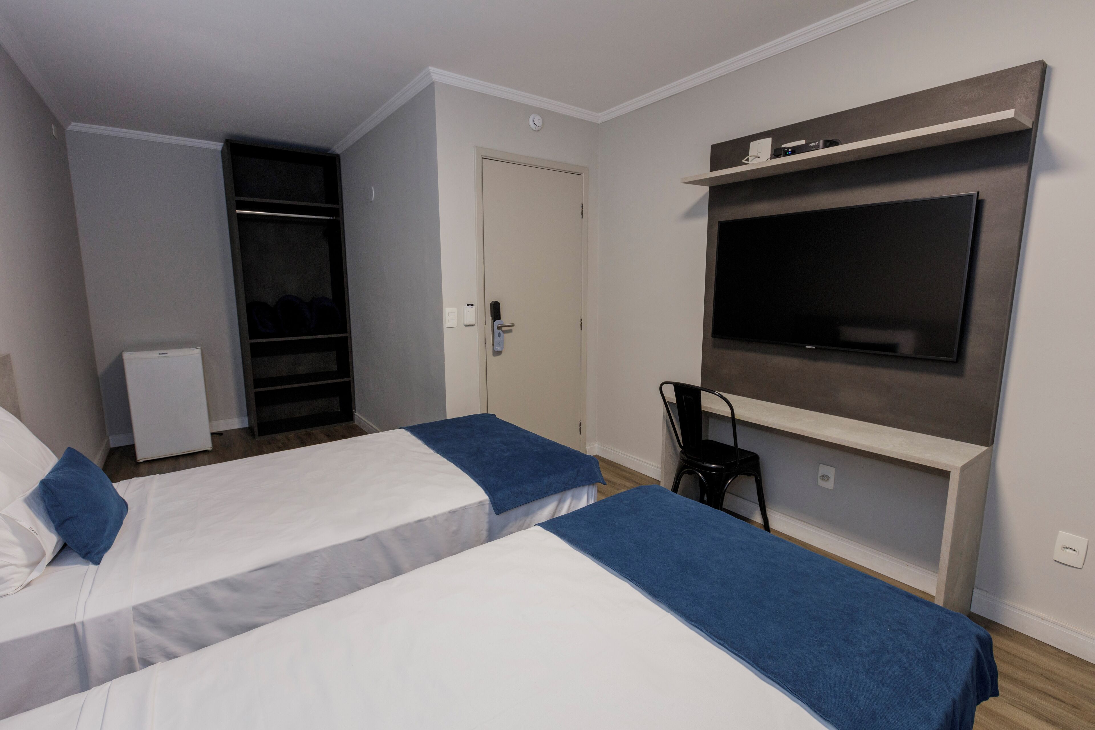 A hotel room with two beds, a TV mounted on the wall, a desk, and a chair.