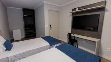 A hotel room with two beds, a TV mounted on the wall, a desk, and a chair.