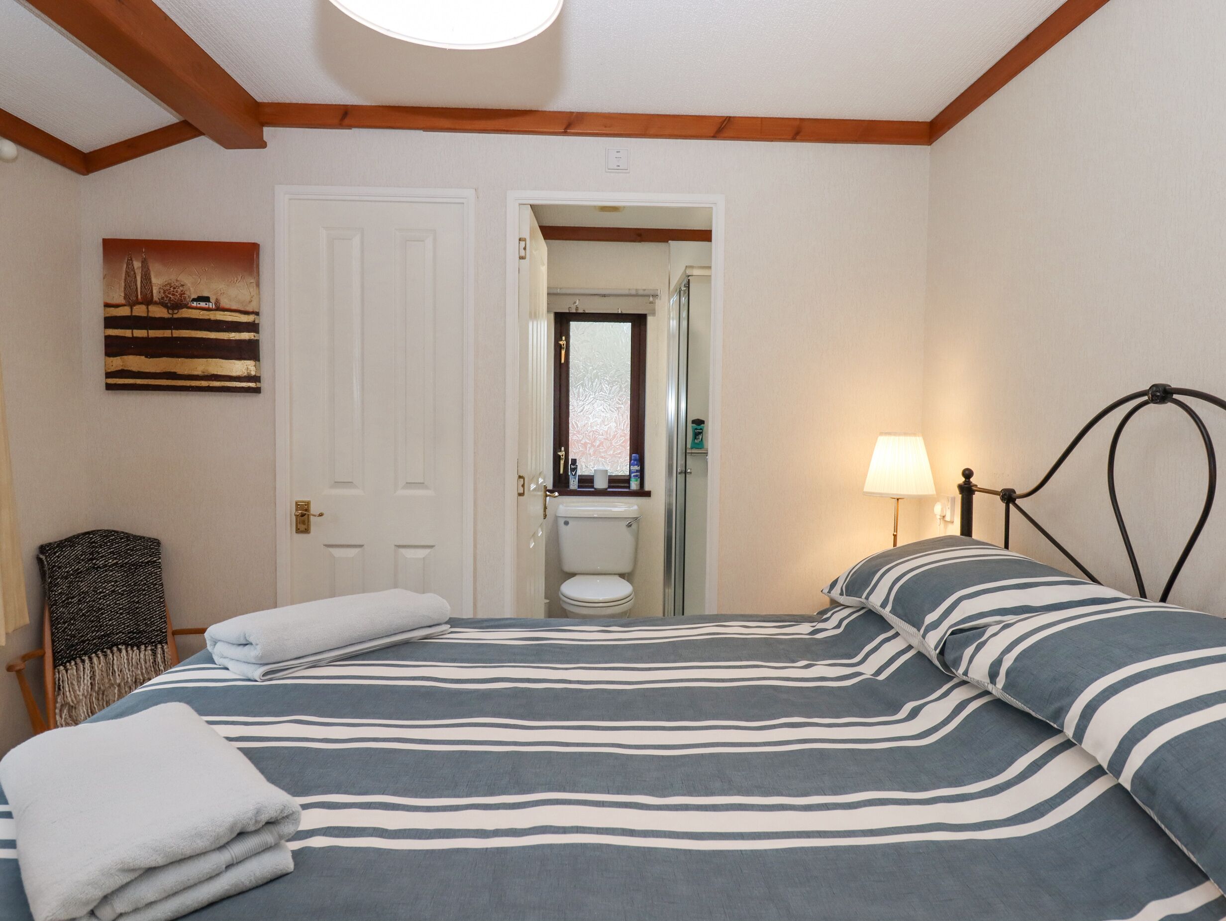 Een slaapkamer met een bed, een stoel, een lamp en een deur die leidt naar een badkamer.