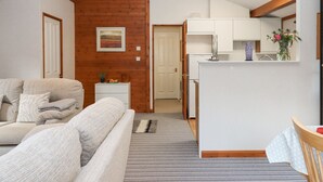 Uma sala de estar acolhedora com sofá, uma mesinha lateral e uma área de cozinha com armários e geladeira.