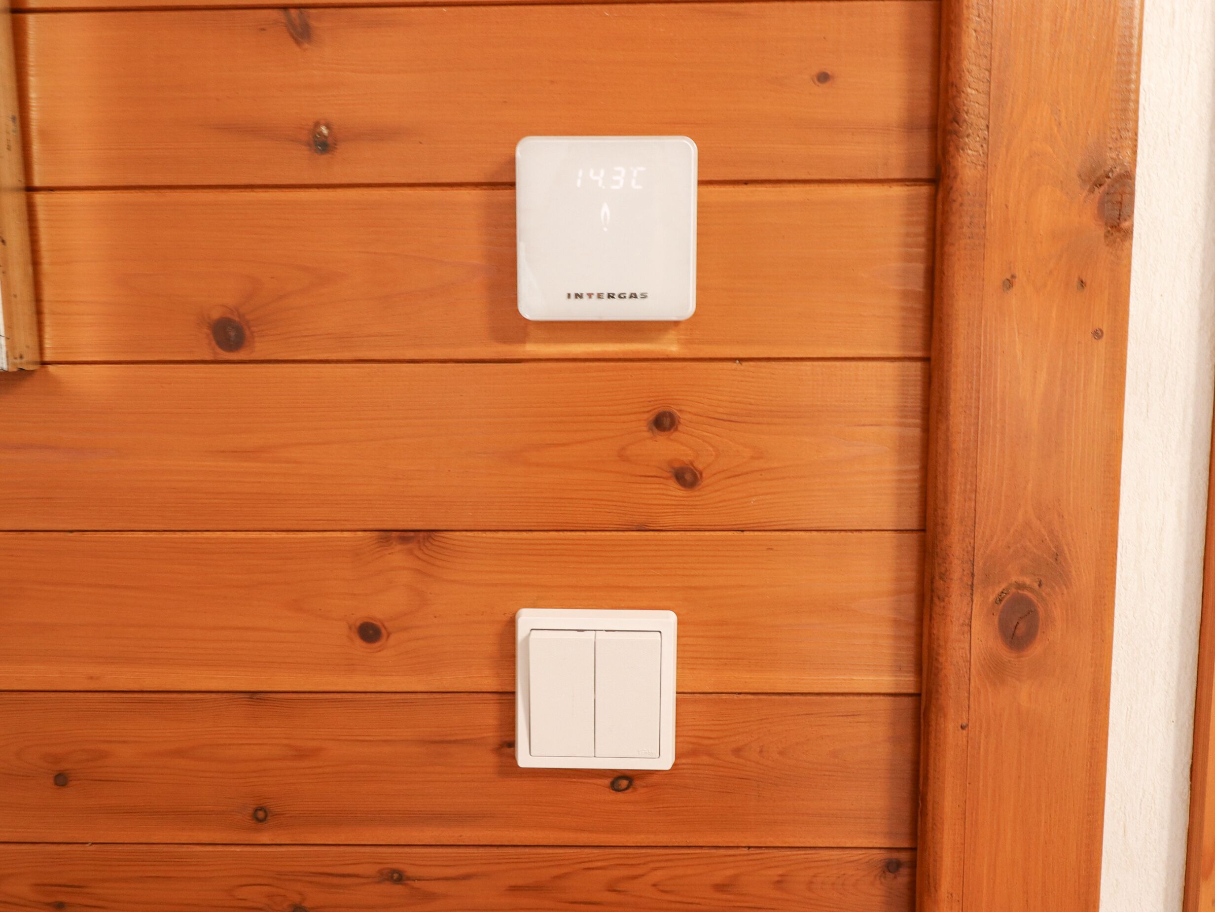 A white thermostat and a white switch on a wooden wall.