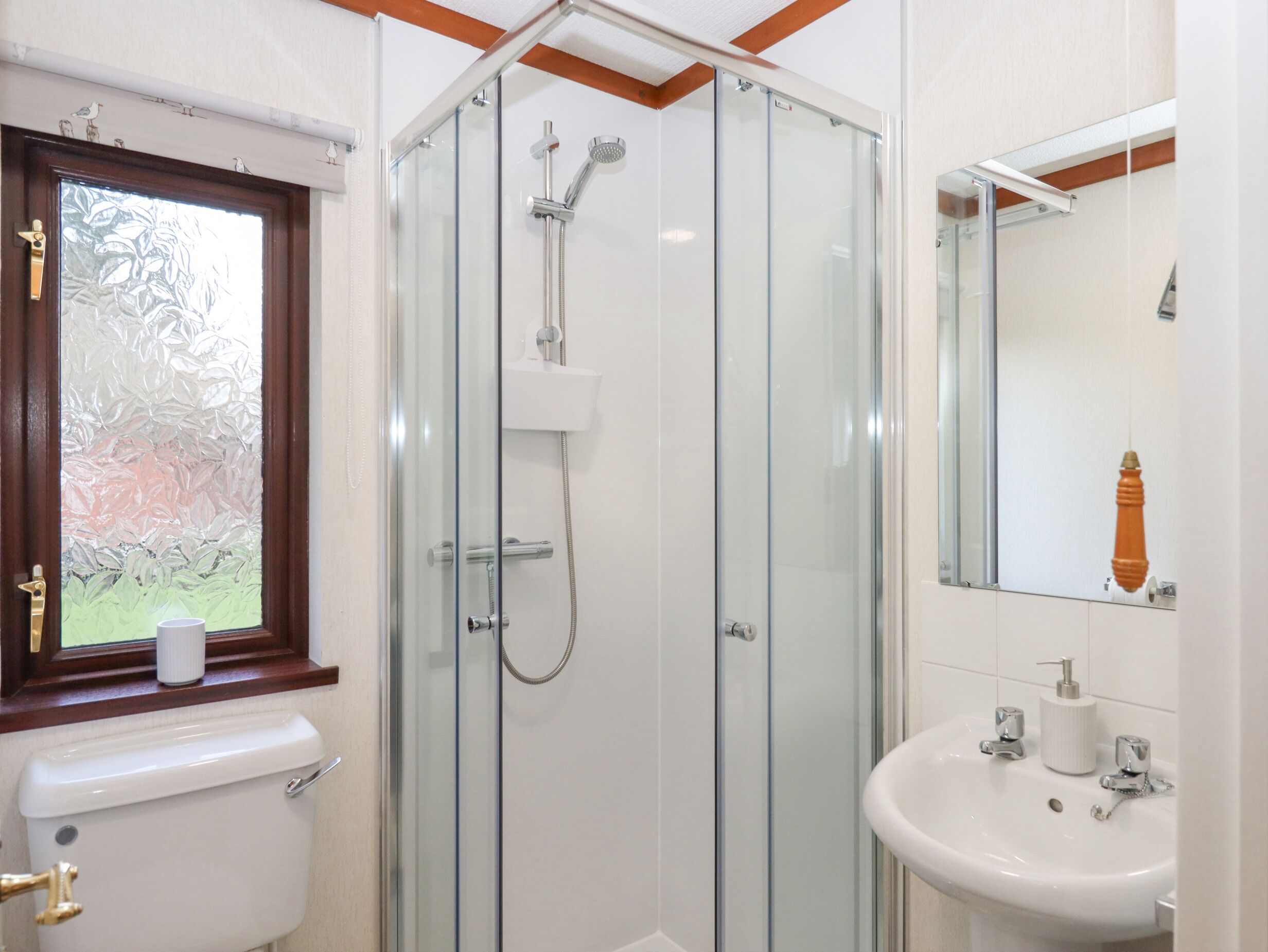 Un baño moderno con ducha de vidrio, lavamanos blanco y ventana con vistas al verdor.