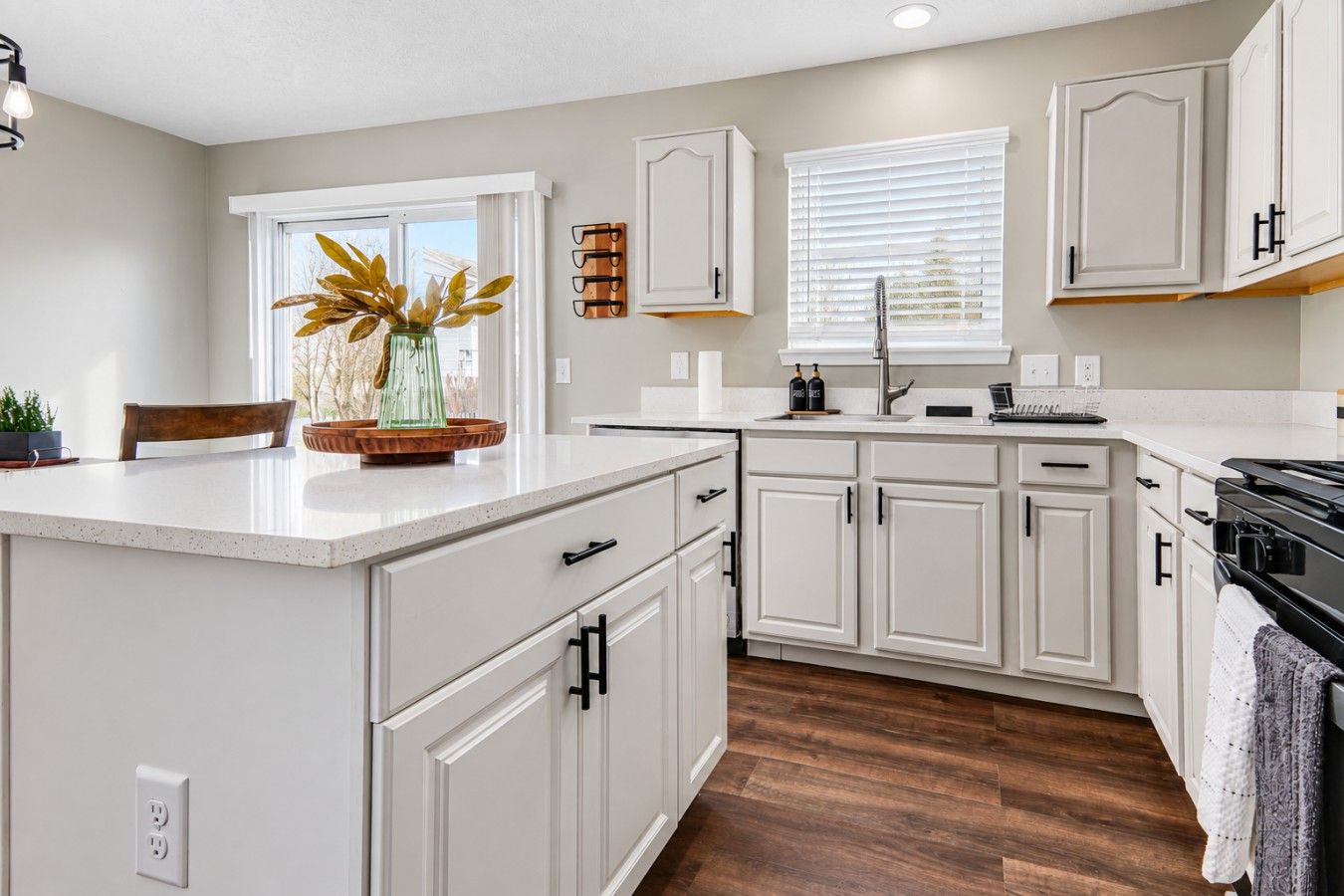 A modern kitchen with white cabinetry, a central island, and a window with blinds.