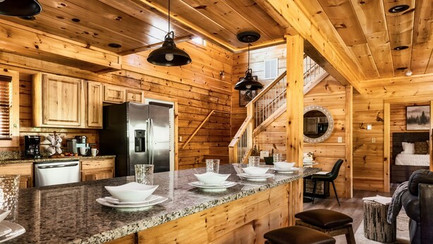 Interior de uma cabana de madeira com cozinha, sala de jantar e escada.