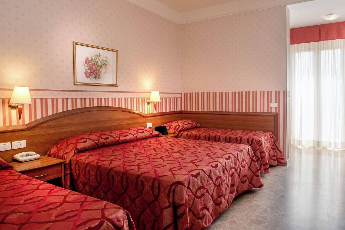 Hotellihuone, jossa on suuri sänky, kaksi yöpöytää, yölamppu ja seinällä taulu.