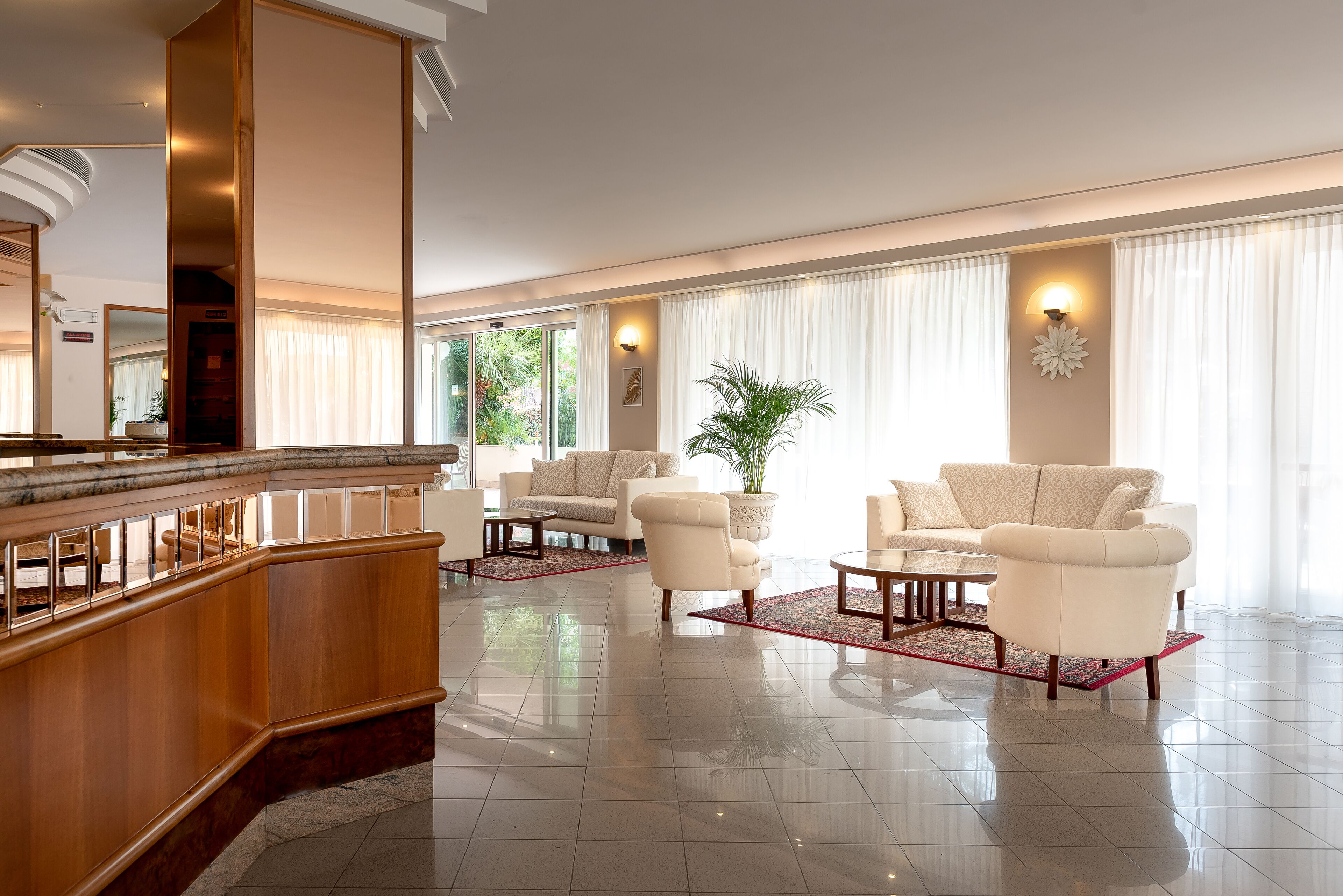 Eine geräumige Lobby mit einem Holzbuchtschreibtisch, zwei Sofas und einer großen Topfpflanze.