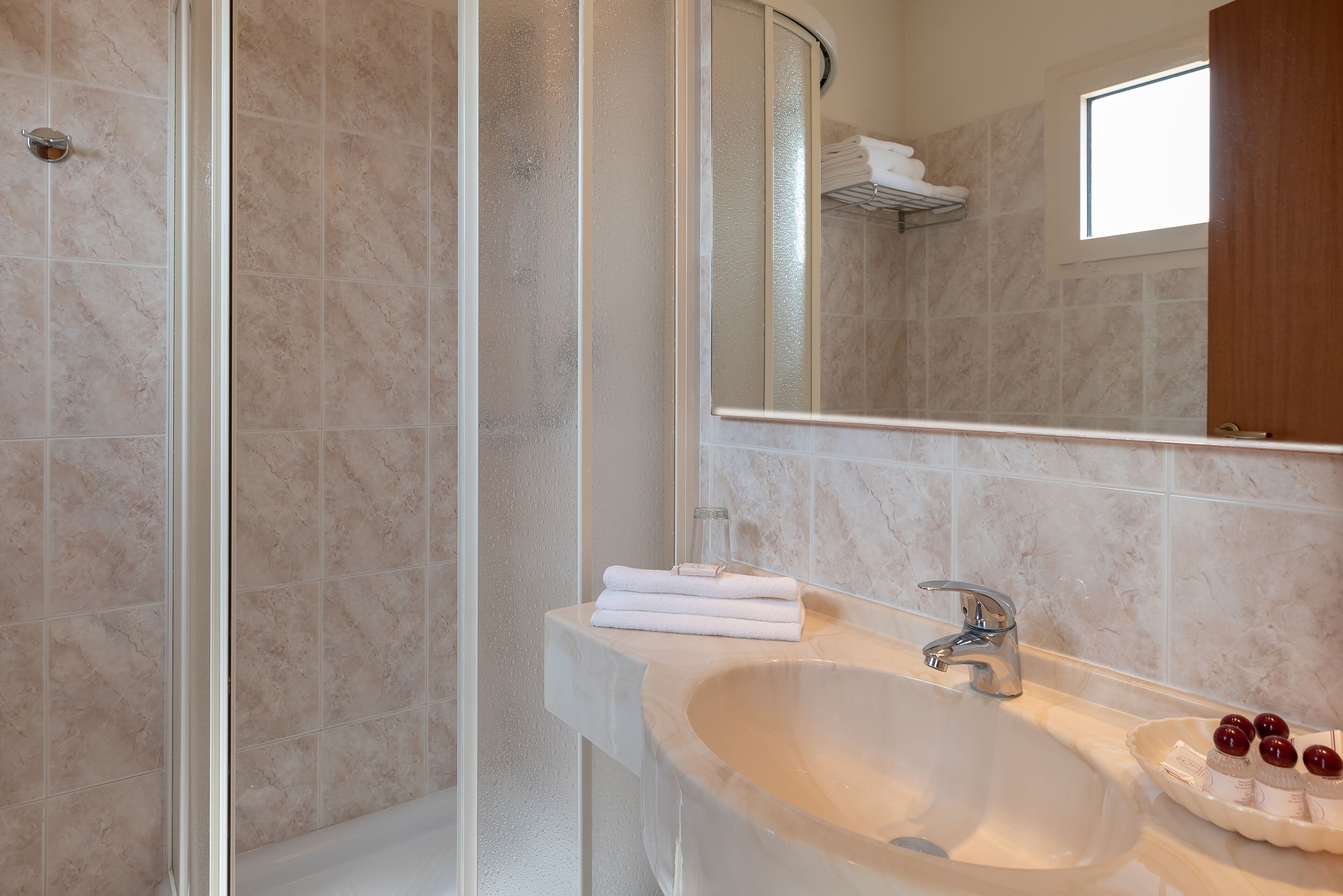 A bathroom with a glass shower enclosure, a sink with a mirror, and a window above the mirror.