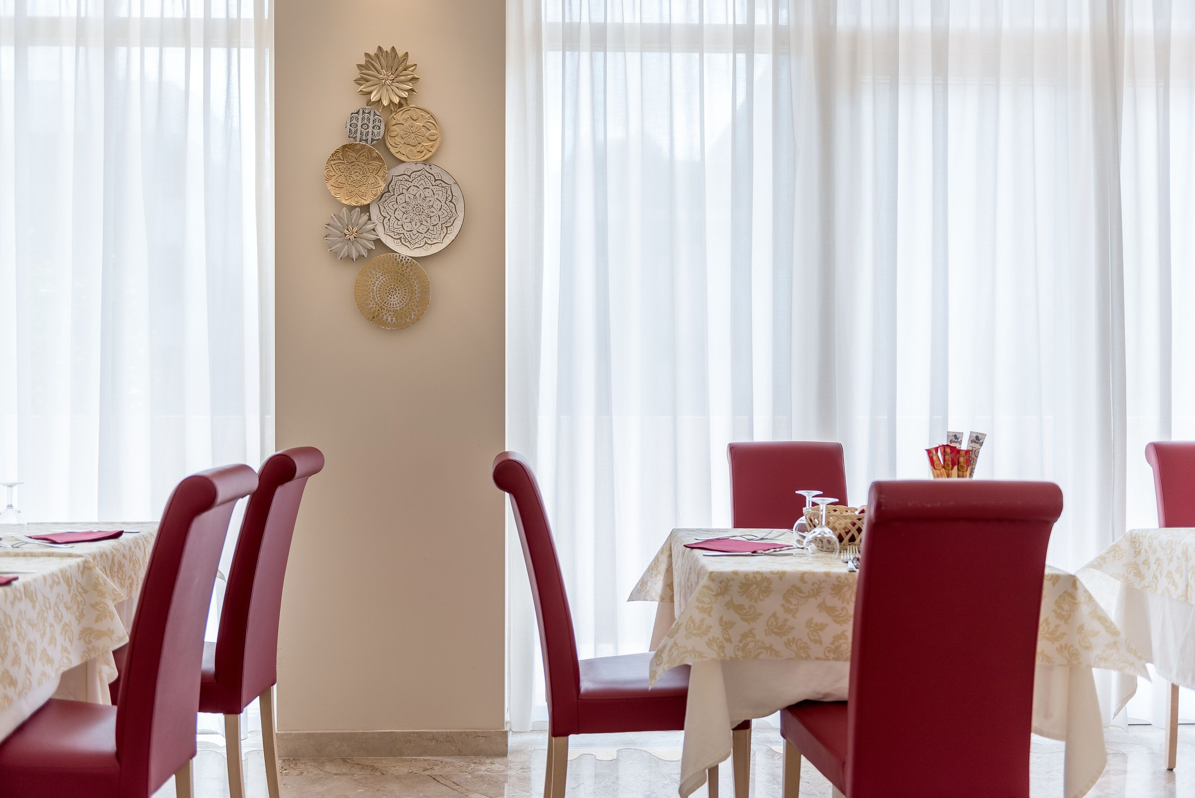 Un espace repas avec des chaises rouges et des nappes blanches, agrémenté d’une décoration murale composée de motifs circulaires.
