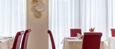 A dining area with red chairs and white tablecloths, featuring a wall decoration with circular patterns.