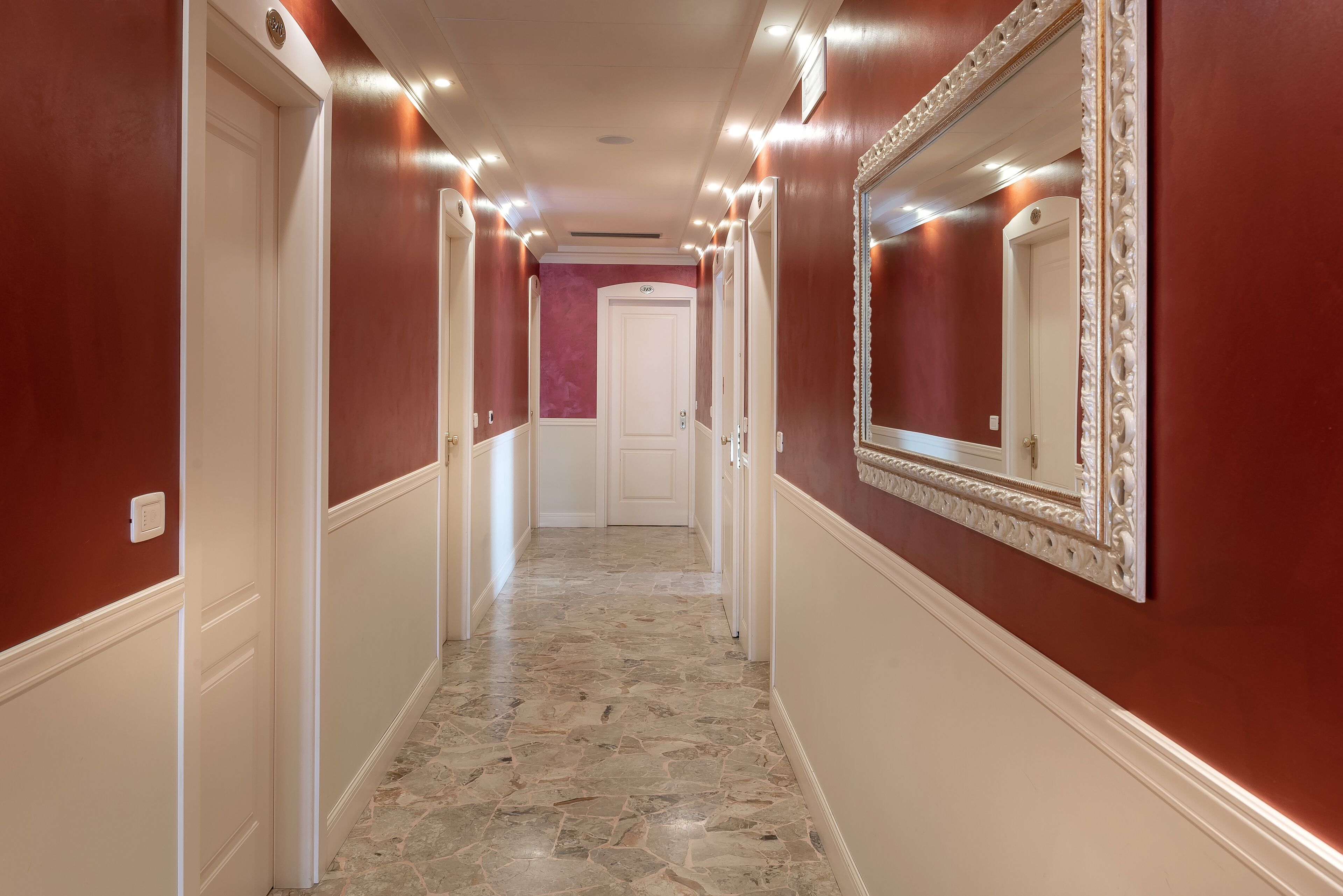 A hallway with red walls, white doors, and a stone floor.