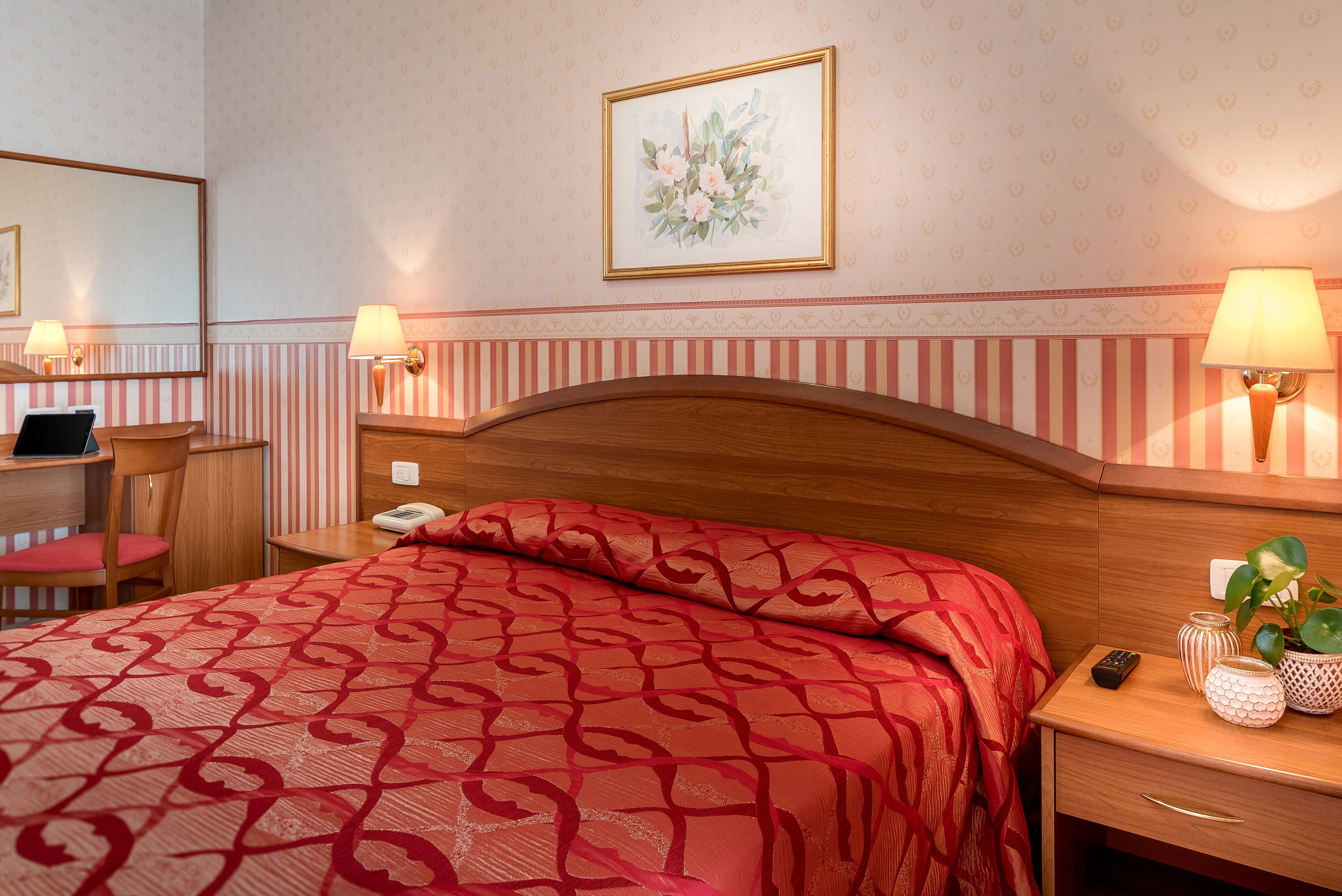 A hotel room with a bed, bedside table, lamp, and a mirror.