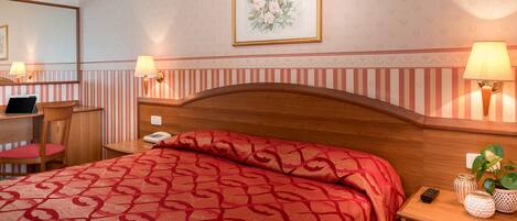 A hotel room with a bed, bedside table, lamp, and a mirror.