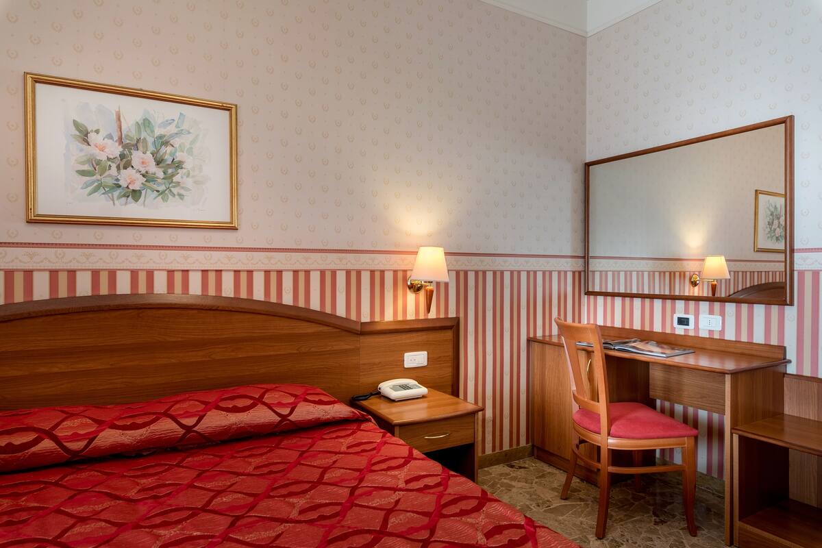 Hotellihuone, jossa on sänky, työpöytä, tuoli ja peili.