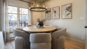 Un coin repas avec une table ronde, des chaises recouvertes d’un tissu gris, un vase central orné de fleurs et trois œuvres d’art encadrées accrochées au mur.