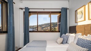 A hotel room with a large bed, a view of a hillside, and a window with curtains. - White Rabbit II by Homie (Calheta)