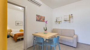 A compact living space with a bed, a sofa, a dining table with chairs, and wall art.