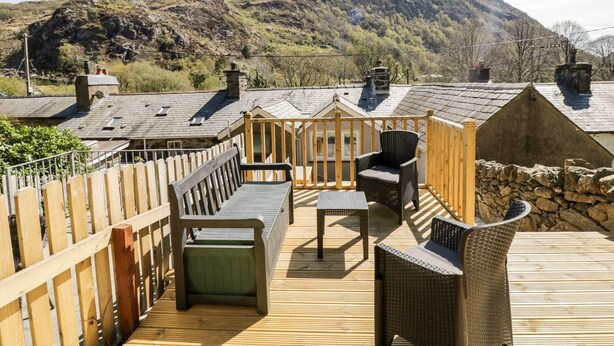 A wooden deck with outdoor furniture, a stone wall, and a mountain view. - Henfro (Caernarfon)