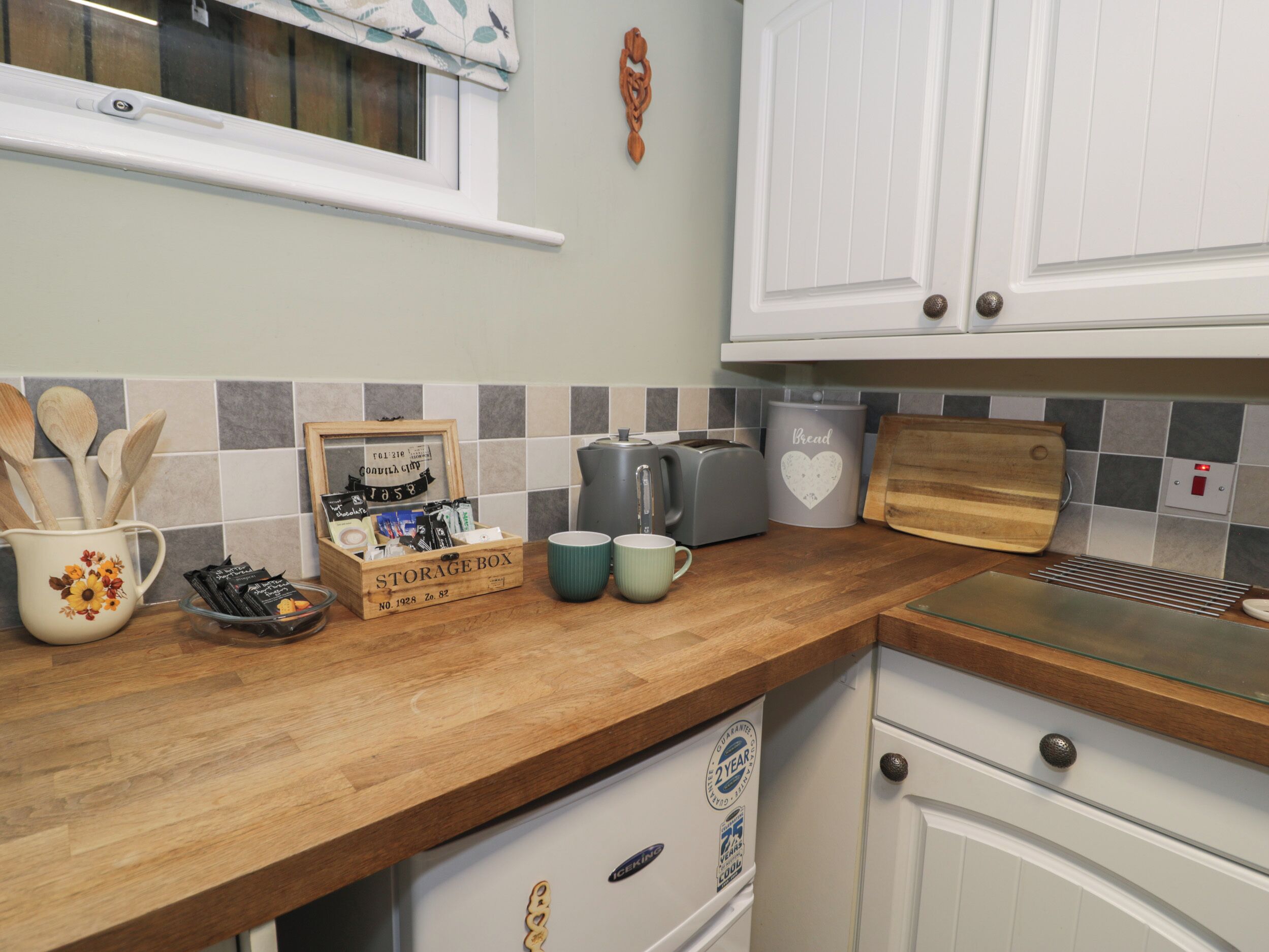 A kitchen with a wooden countertop, a storage box, a coffee maker, a toaster, and a bread container.