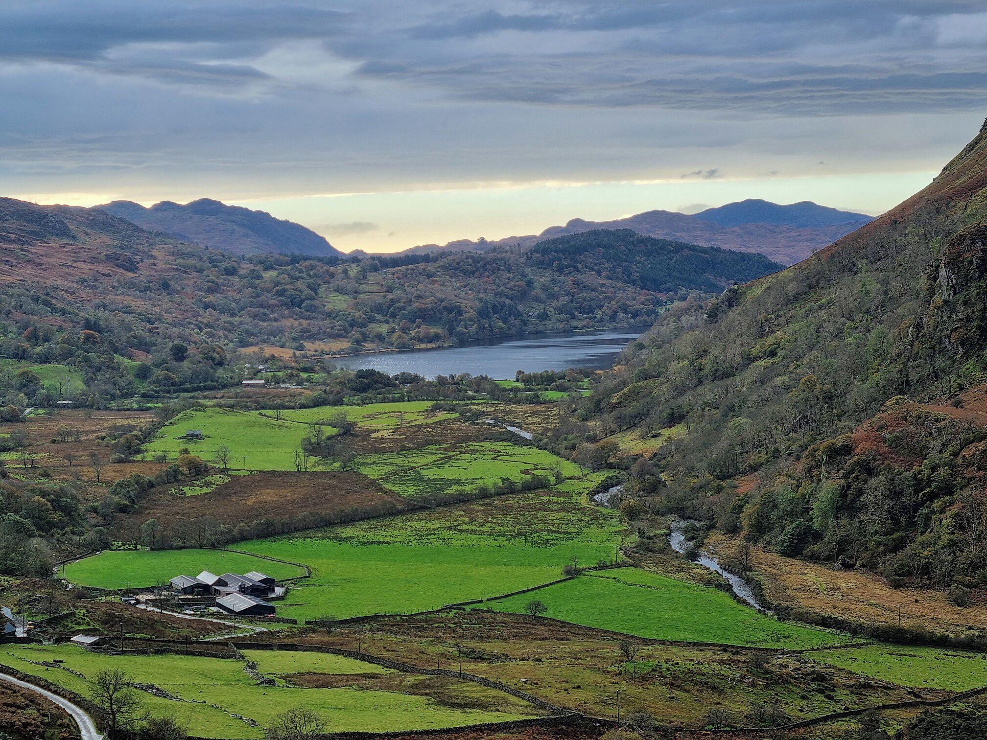 A valley with a lake, green fields, and a small building.