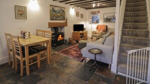 A cozy living room with a fireplace, a dining table, and a staircase. - Henfro (Caernarfon)