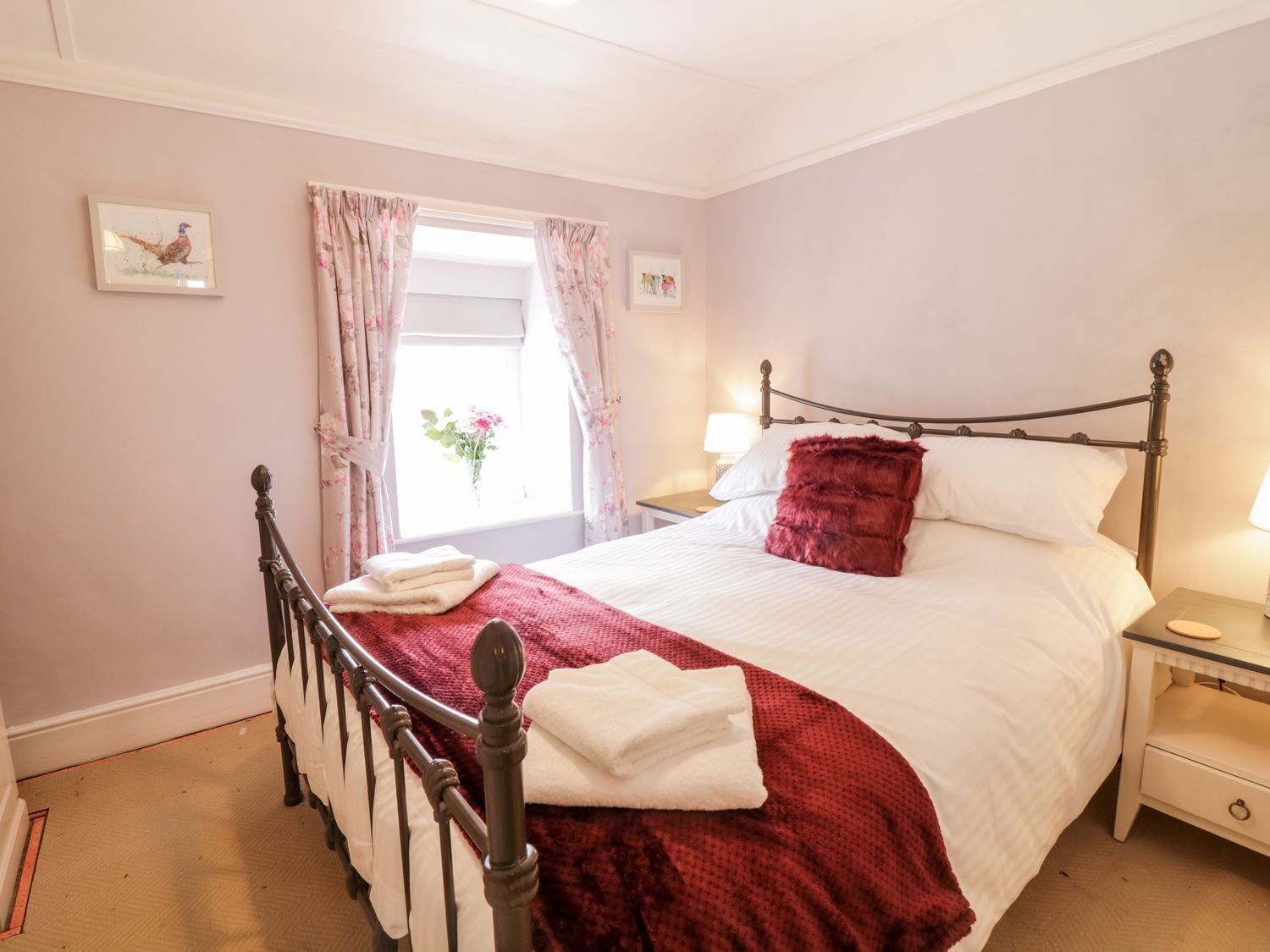 A bedroom with a bed, a nightstand, a window with curtains, and a picture on the wall.