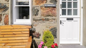 A stone building with a wooden bench and a door. - Henfro (Caernarfon)