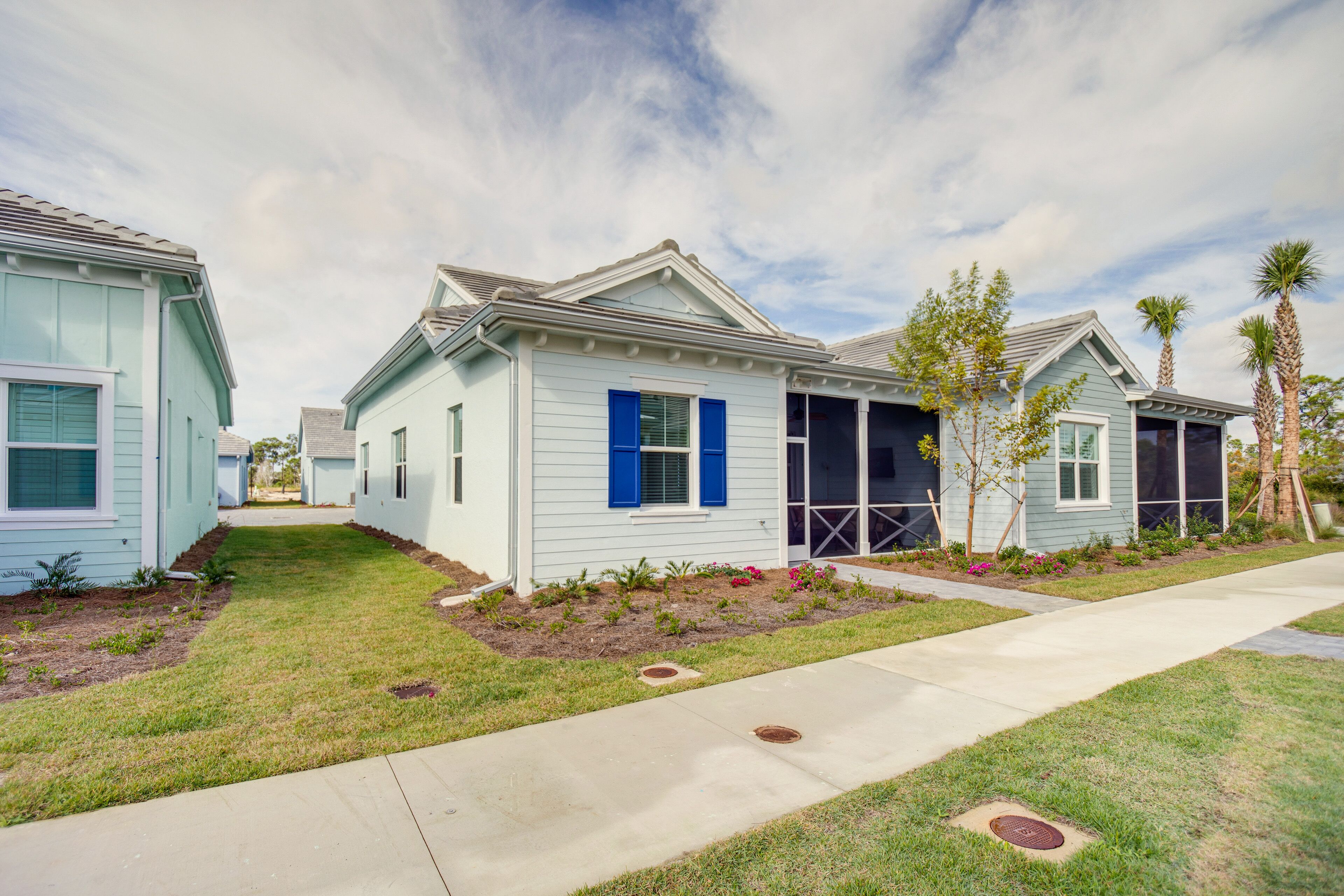A row of light blue houses with blue shutters, a sidewalk, and small trees.